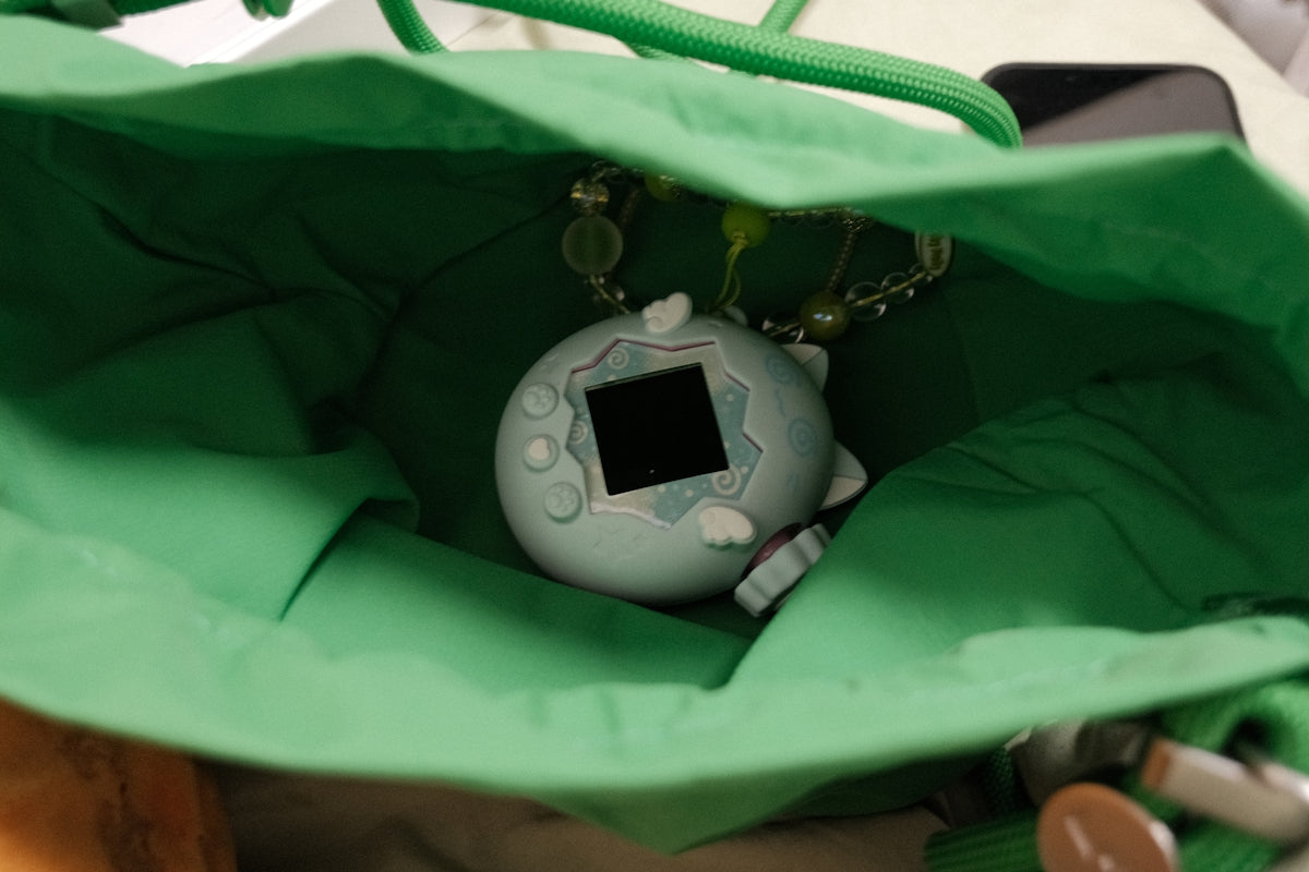 A light blue tamagotchi virtual pet inside a green bag