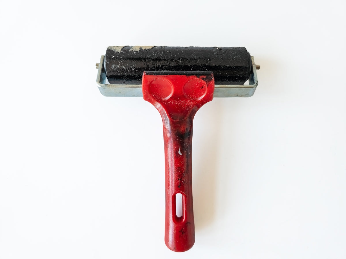 A red-handled brayer with a black roller on white